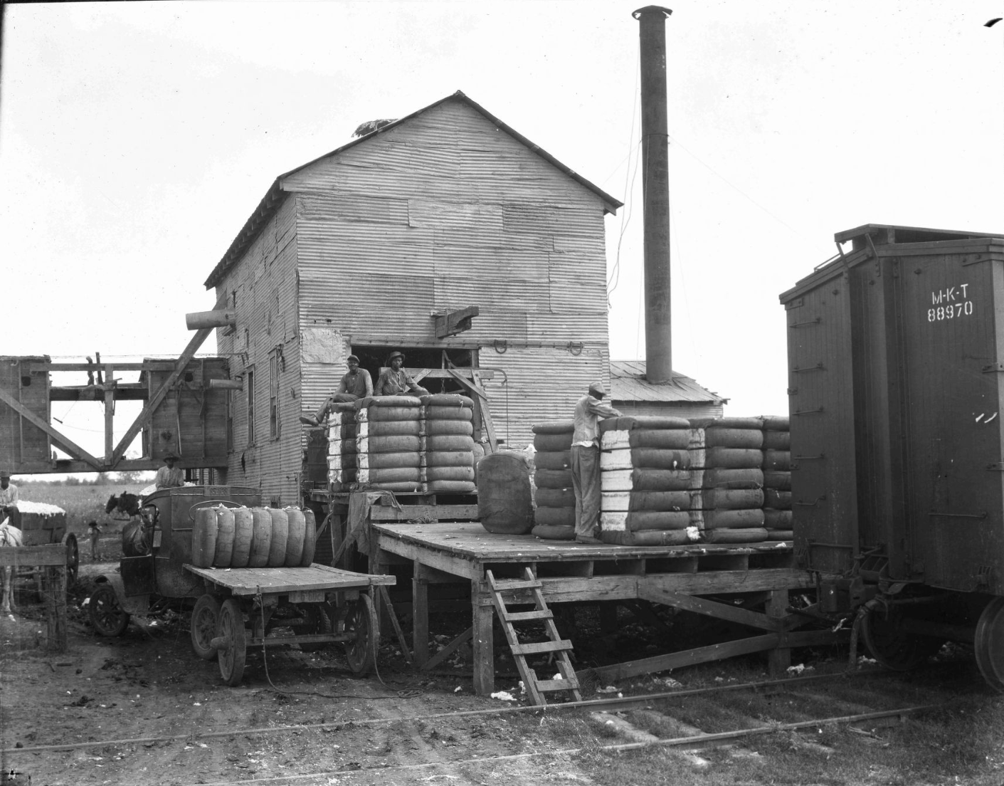 Three Black men loading bales of cotton onto a railcar