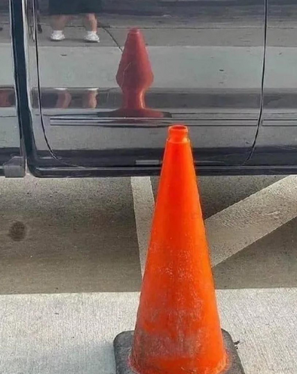 Traffic cone that looks like a butt plug in its reflection.