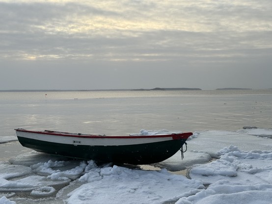 Fisherman’s small boat pulled on ice, behind it calm sea and some islands on the horizon