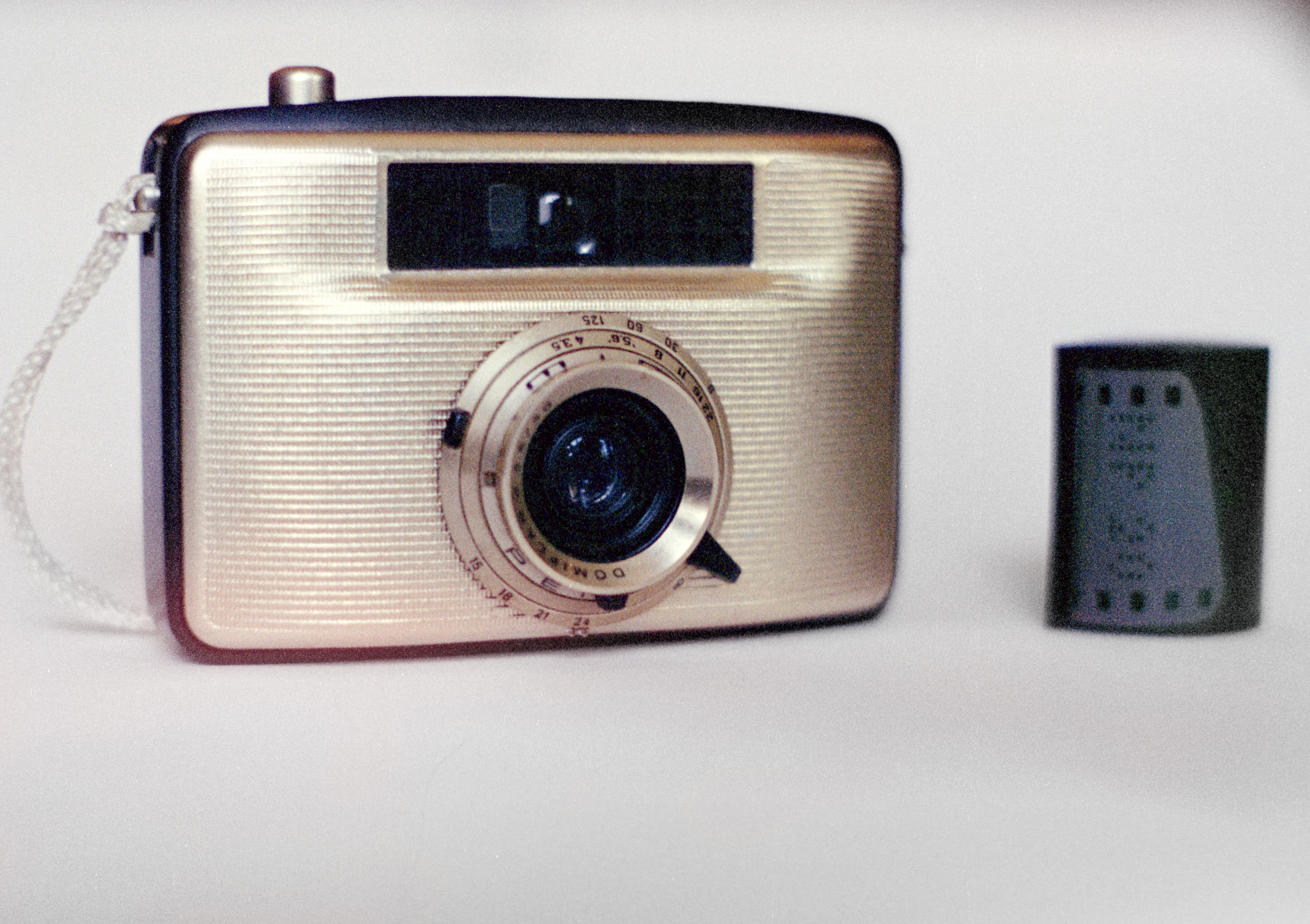 a small gold-coloured film camera next to a small film canister.
