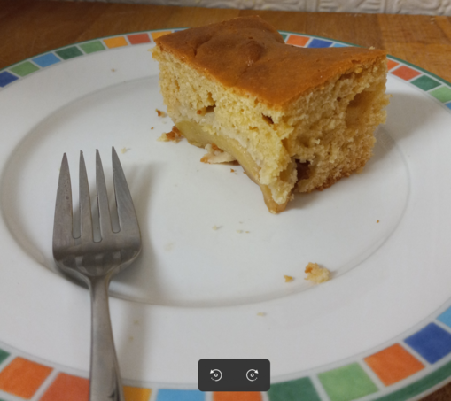 A photo of a piece of cake on a plate with a fork. Crumby cake covers a crosscut apple.