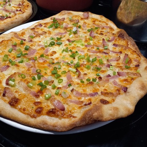A pizza with cheese, bacon, and green onions on a white plate.