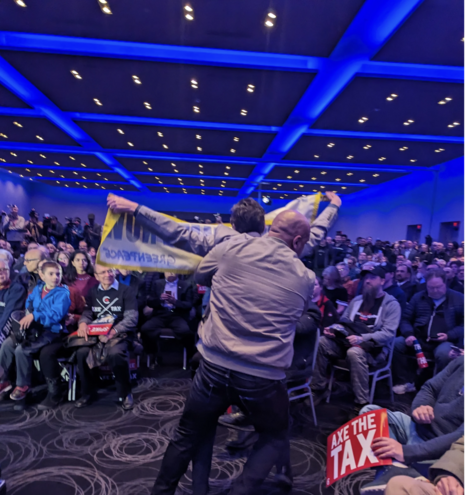 A man holding up a banner is removed from a meeting by a security guard

© Griffin Stewart-Wilson. After raising his “Act on Climate Now” sign, Greenpeace Canada climate strategist, Keith Stewart was swiftly removed from the Conservative party ‘Axe the Carbon Tax’ rally by security.
