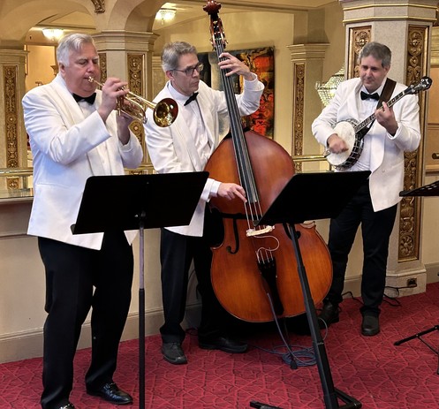 Three men in white tuxedos playing traditional jazz - trumpet, string bass and banjo