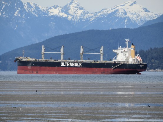 "Ultra Passion" an Ultrabulk bulk carrier at anchor in the Burrard Inlet with some mountains in the background some of which still have some snow cap