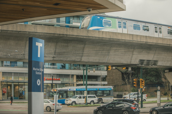 Marine Drive Station in Vancouver with a Canada Line train arriving and a hybrid bus visible in the background.