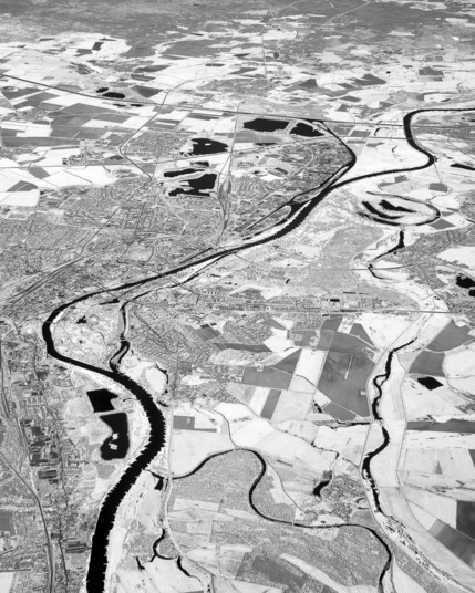 A black river winds through a white patchwork of fields and a big town