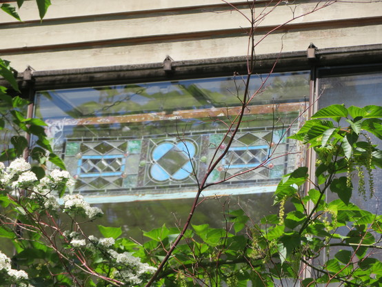 A small row of three decorative stained glass windows behind a match larger clear window pane