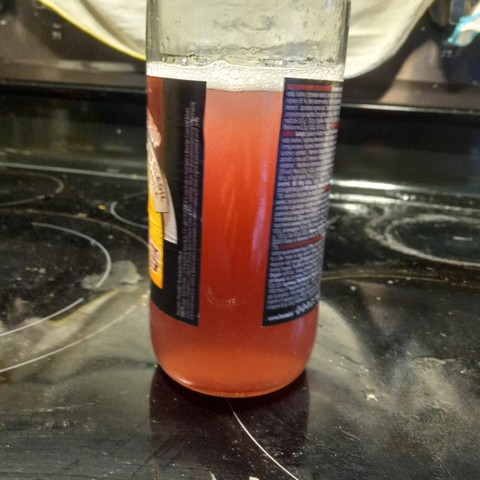 A glass bottle two-thirds full of red liquid.