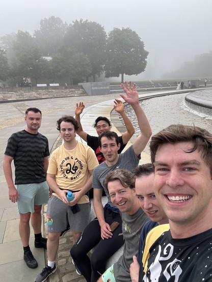 Seven sweaty smiling people sitting at the edge of a large fountain after a 5k run. 