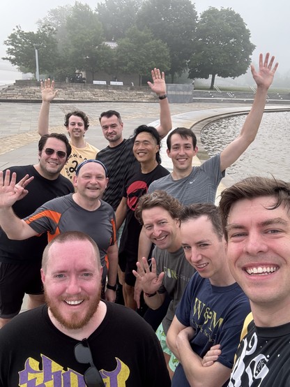 Ten sweaty smiling people sitting at the edge of a large fountain after a 5k run. 