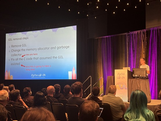 Anthony Shaw standing on stage behind a podium at the right, with a slide on the left titled "GIL removal steps".

1. Remove GIL
2. Change the memory allocator and garbage collector
3. Filx all the C code that assumes the GIL existed