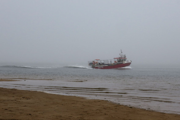 Fishing boat 'Charlie John' just off the beach running into harbour in fog, nice wake  in channel with shallow water breaking onto the beach in the foreground, muted colours