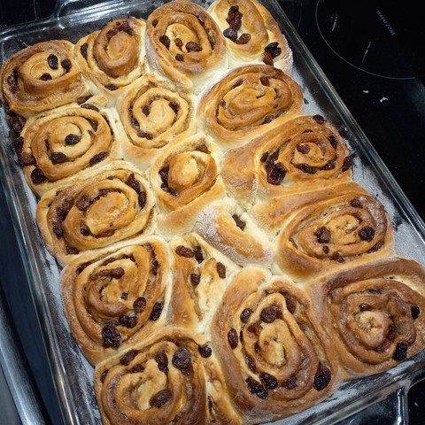 A pyrex cake pan on a stove top full of golden-brown cinnamon rolls.