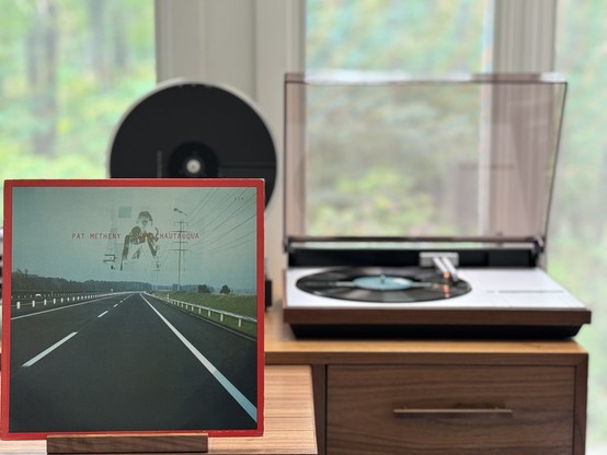 Pat Metheny - New Chattaqua LP cover.

A road shot from on the road, in the right lane heading straight into the distance, guard rails on both sides.

The black LP plays on a vintage Bang & Olufsen Beogram 4000 linear-tracking turntable to the right.