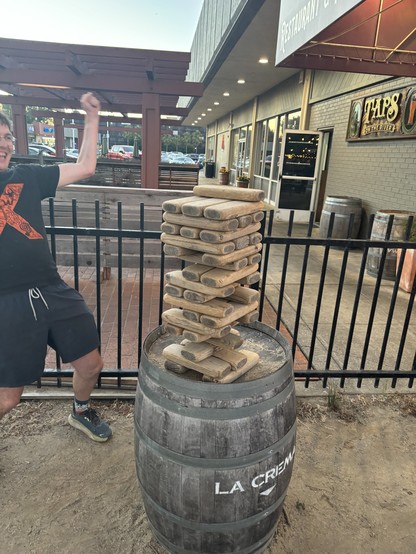 A person cheers as they successfully balance a wooden block on a tall and precarious stack. 