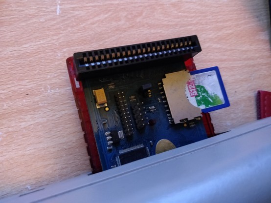 MMC64 board in translucent red half-case in cartridge port of C64, with well worn SD card poking out the side.