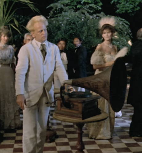 screenshot from fitzcarraldo. klaus kinski is aggressively playing opera on his phonograph at a party and is about to be forcibly removed from the premises 