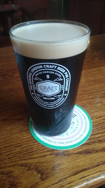 A black pint of London Black beer with a white head in a straight glass and branded Craft Beer Company 