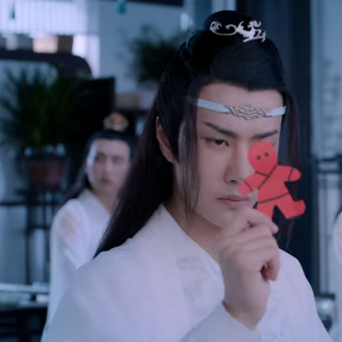Closeup of Lan Wangji holding a red paperman talisman in his fingers. He is stearing at the talisman angrily