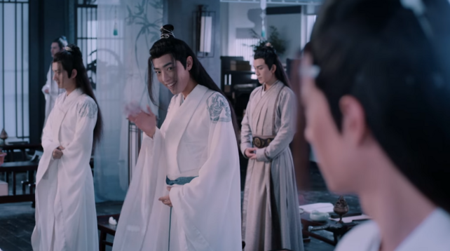 Wei Wuxian waving at Lan Wangji innclass room at Cloud Recesses. He's wearing white robes, just like Nie Hiaisang who's standing behind him. Also Meng Yao standing behind him in light robes