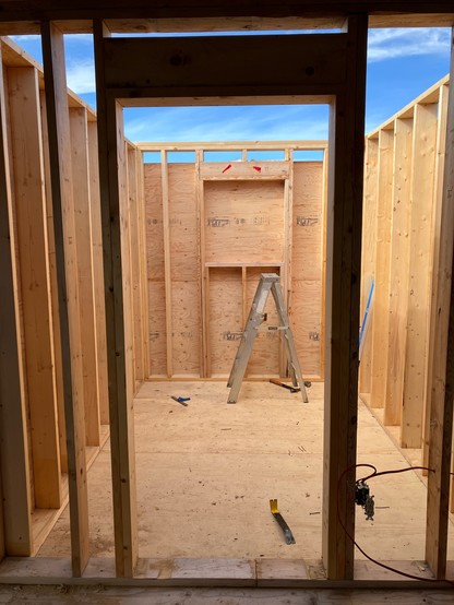 Looking out a newly framed door at the interior of an unfinished addition to the cabin. Studs and plywood. 
