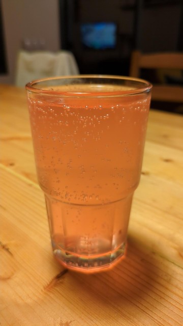 A pinkish fizzy drink ina clear glass on a wooden table.