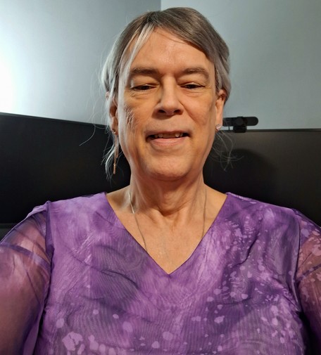 Selfie of an older white trans woman. Janet is wearing a gray / silver ombre wig, with a blouse in 