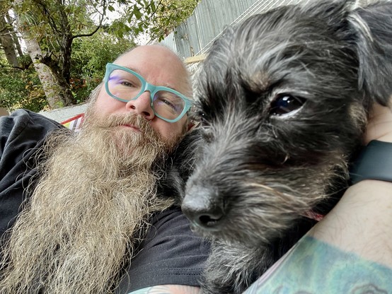 Lying on a hammock with Lola. I have a long beard and teal glasses. She is a short haired chihuahua terrier mix. She lying in the crook of my arm.