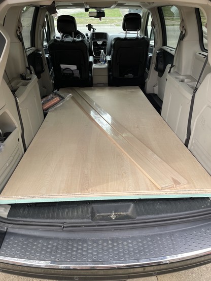 Photo from rear door of minivan showing two long boards, and two sheets of plywood  plus and insulation panel, both rows of rear seats have been folded down, but it still fits completely within the doors