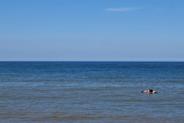 A calm blue sea and a bright blue sky, two people drifting in the sunshine on an isolated paddleboard