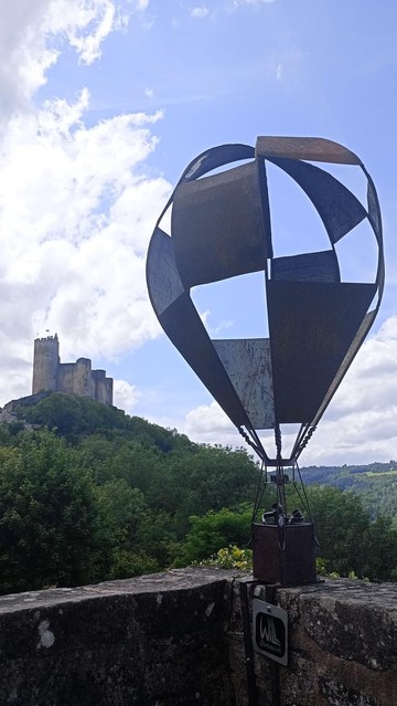 A metal sculpture of a hot air balloon with a castle on a hill behind under blue skies