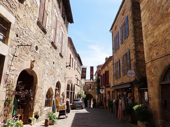 A narrow street lined with tall stone buildings with pretty shops decorated with bright flowers