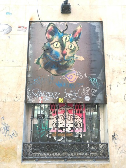 Ventana similar, pero la pieza de arte urbano es la cabeza de un gato oscuro con 3 ojos