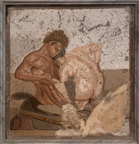 An image of a man and a woman having sex. Both are naked, the man sits upright on a bed and the woman faces him and leans into him as they embrace. The man looks stern, and the woman has her eyes closed. The man has dark skin, and the woman light skin. The work is done in the opus vermiculatum style so the figures are highly detailed and delicately shaded and colored.