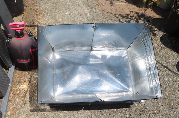 Elliptical plastic tank covered in black material on the left. It's a Reliance solar shower. To the right is the SOS Sport solar box oven with coroplast reflectors deployed.