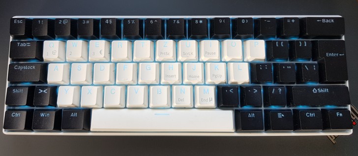 A keyboard with four rows of keys and without arrow keys. Keys A-Z and the spacebar are white, all other keys are black. Mix of German and American layout. Blue keyboard backlight.