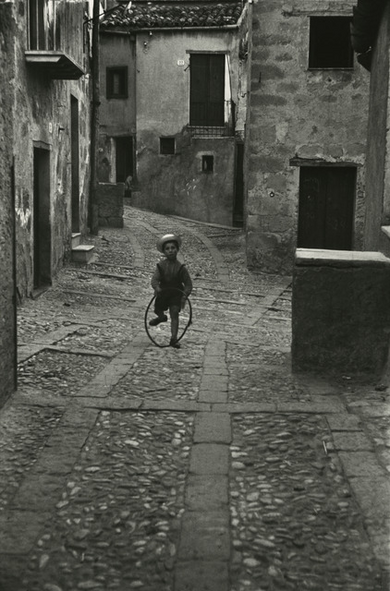 Photograph of a boy walking in a narrow street with a barrel hoop.