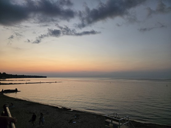 The water is like glass. Like dark smokey glass with some reflectionof the pastel horizon. The Sun is below the horizon. The camera is pointed at WNW. The sky is dark at the horizon. Above the horizon, we get pastel oranges followed up with blue- grey