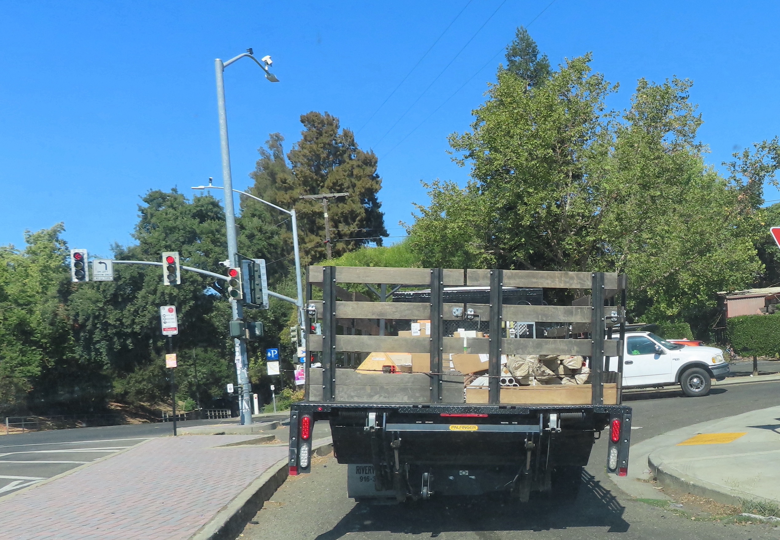 Truck with wooden slat sides. The space where a license plate should be is empty. It is in the right hand slip lane, about to turn right in Davis, California.