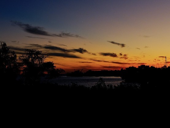 Photo of a sunset over a lake, warm red fading to blue, with the foreground in shadow.