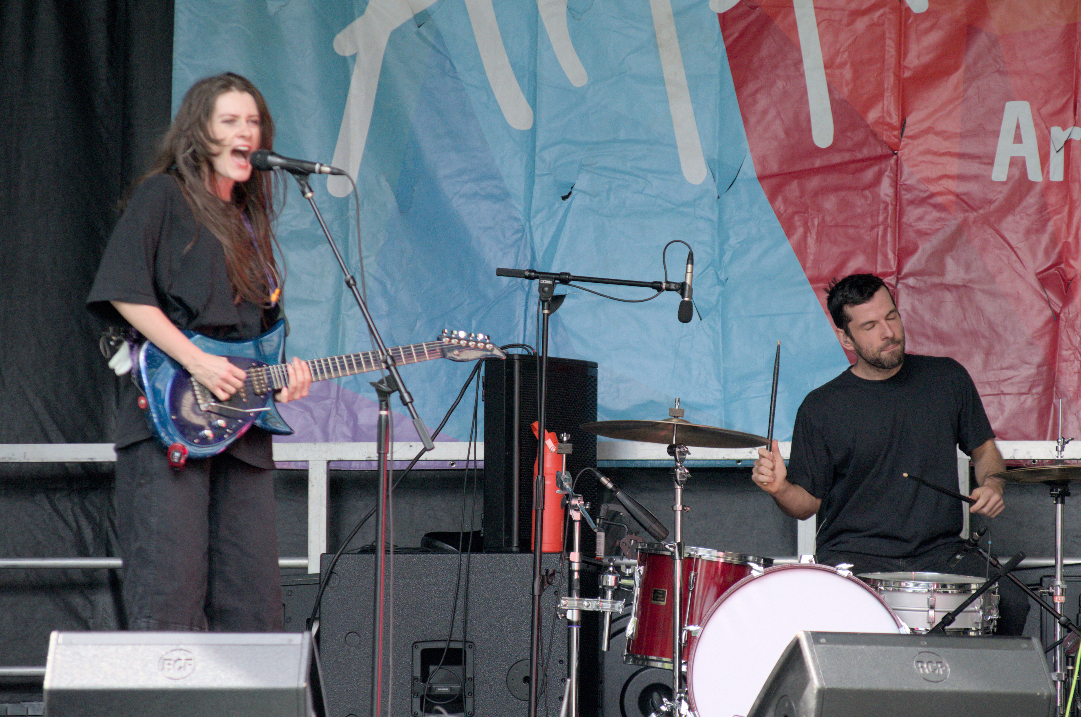 A guitarist and a drummer playing onstage, the guitarist is singing and the drummer has his eyes closed as he plays.