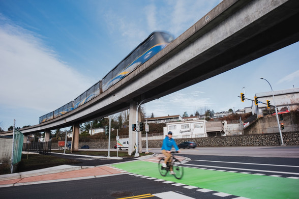 A stretch of overhead track used by SkyTrain over a road junction with a bike lane in green and a cyclist crossing 