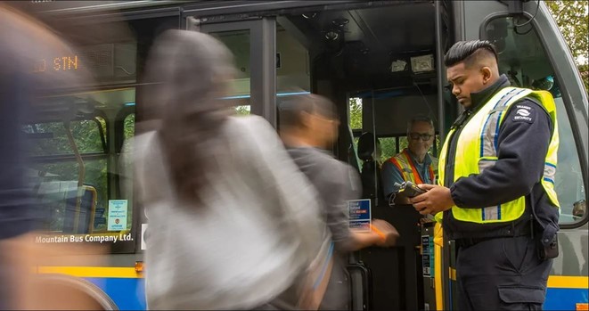 A uniformed male officer wearing a hi vis vest checks compass cards as people board a bus