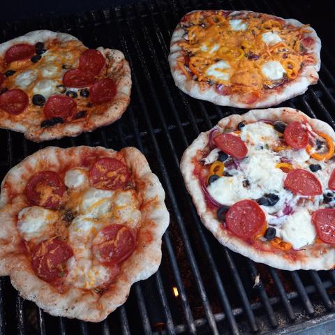 Four small pizzas, one made by each member of the family, cooking on a barbecue. 
