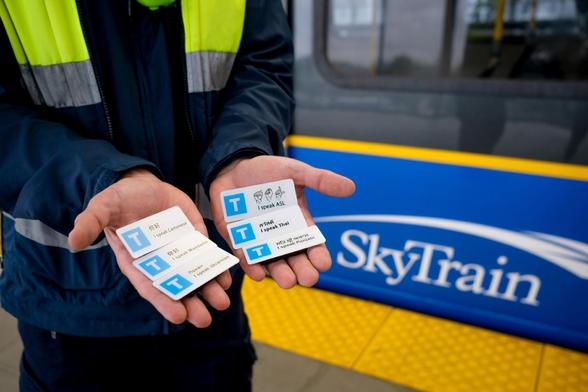 A man holding out his hands palm upwards - on each are three small badges with a large capital T and the name of the driver and the language he or she speaks
