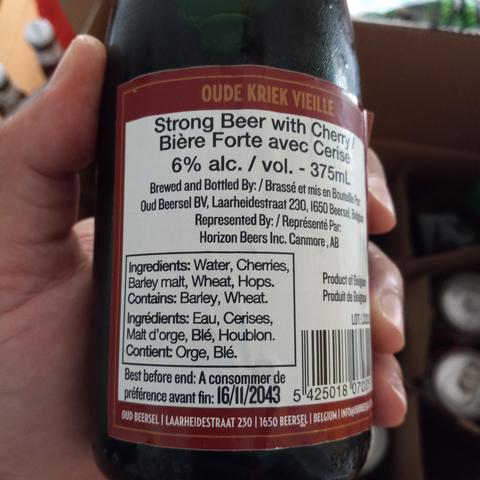 A white hand holding a bottle of Oude kriek vielle. On the back label, among other information, is the best-before date: 16/11/2043.