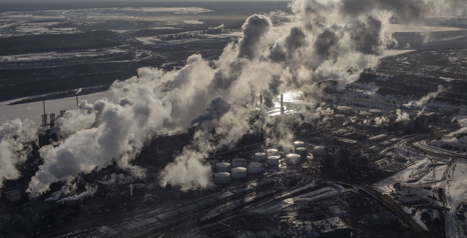 A monochrome aerial image of fossil fuel exploitation - lots of active chimneys  belching air pollution