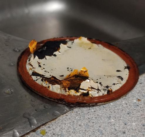 An upside down mason jar lid on a stainless steel sink. The plastic coating is peeling and the lid is nearly rusted through.
