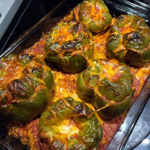 A transparent pyrex baking dish full of baked rice, tomato sauce, and six stuffed green peppers. 